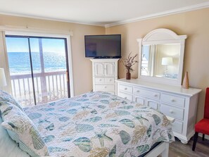 Een slaapkamer met een bed, een dressoir, een televisie en uitzicht op de oceaan door een schuifdeur.