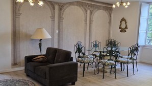 Ein Wohnzimmer mit einer Couch, einem runden Tisch mit Stühlen, einer Lampe und einer Wand mit Verzierungen und Bögen.