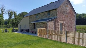 Ein Steinhof mit geneigtem Dach, einem eingezäunten Hof und Außenbestuhlung.