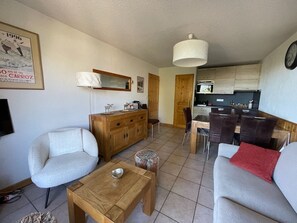 A living room with a sofa, a coffee table, and a dining area with chairs and a table. - 2-bedroom apartment, ski-in/ski-out, parking, sleeps 6 (Les Carroz d'Arâches)