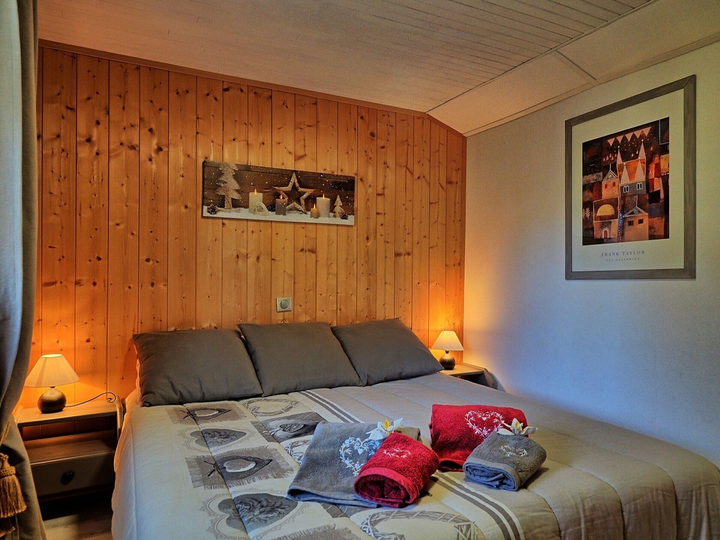 Une chambre d’hôtel avec un mur lambrissé en bois, un lit avec plusieurs oreillers, une table de chevet avec une lampe et un tableau encadré au mur.