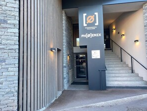 A modern building entrance with a stone facade, a wooden slatted wall, and a staircase leading inside. - Apartment in Courchevel Village center with WiFi (Courchevel 1550)