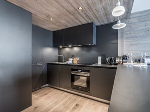 A modern kitchen with dark cabinetry, a wooden ceiling, and a built-in oven. - Apartment in Courchevel Village center with WiFi (Courchevel 1550)