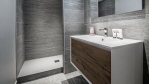 Un baño moderno con un espejo grande, un tocador de madera y paredes con azulejos grises.