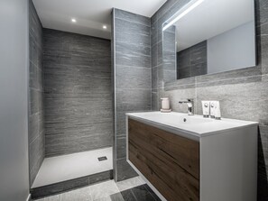 A modern bathroom with a large mirror, a wooden vanity, and grey tiled walls. - Apartment in Courchevel Village center with WiFi (Courchevel 1550)