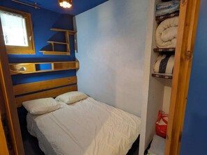 A small, compact bedroom with a bunk bed and a single bed, wooden headboard, a window with a curtain, and a shelf with folded blankets. - Cozy apt for 4, near slopes and pool (Arêches-Beaufort)