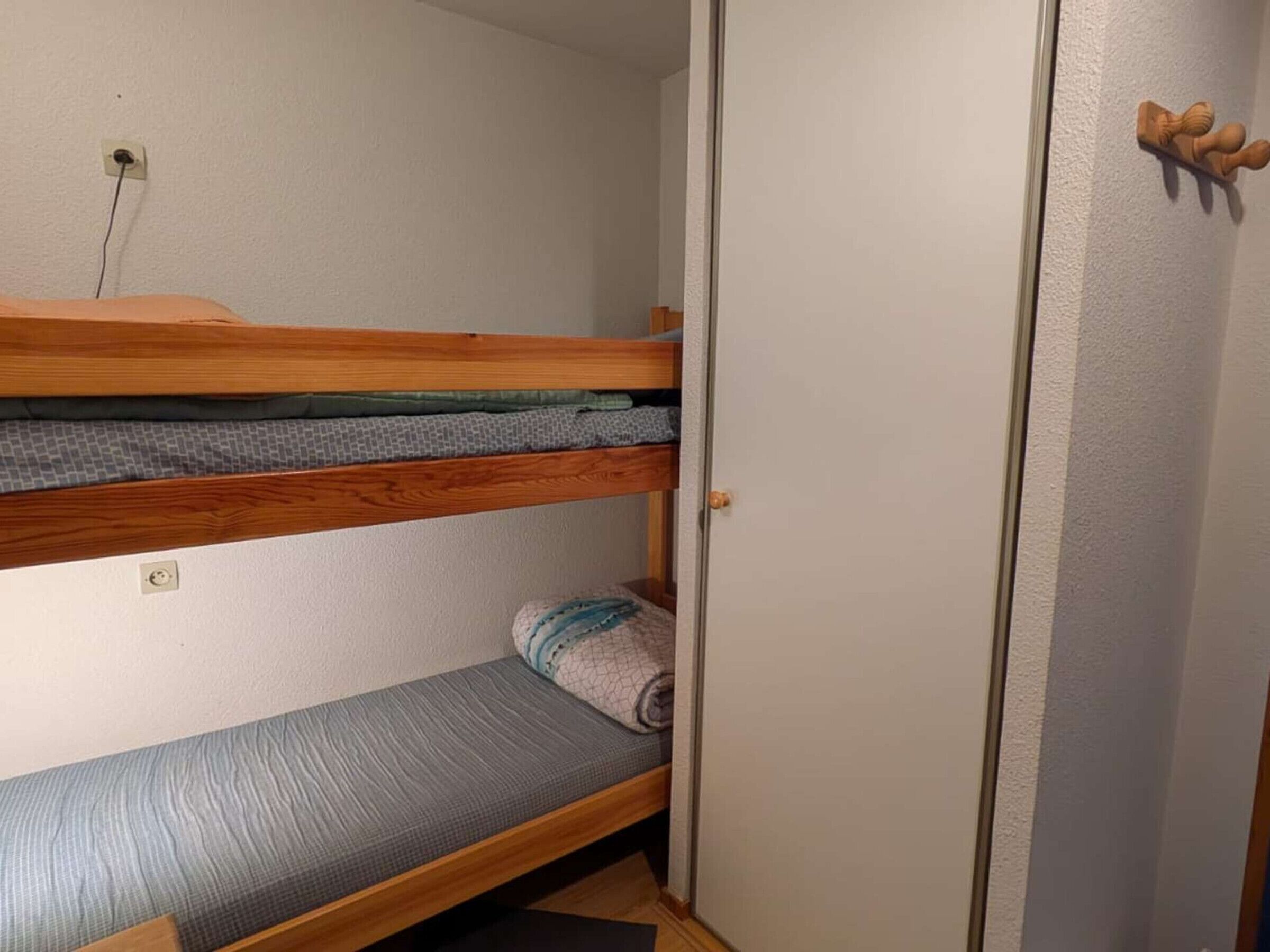 Une petite pièce, de taille modeste, comprenant un lit superposé et un lit simple. On y trouve une porte en bois avec une poignée, ainsi qu’une petite étagère sur laquelle est posé un objet décoratif.