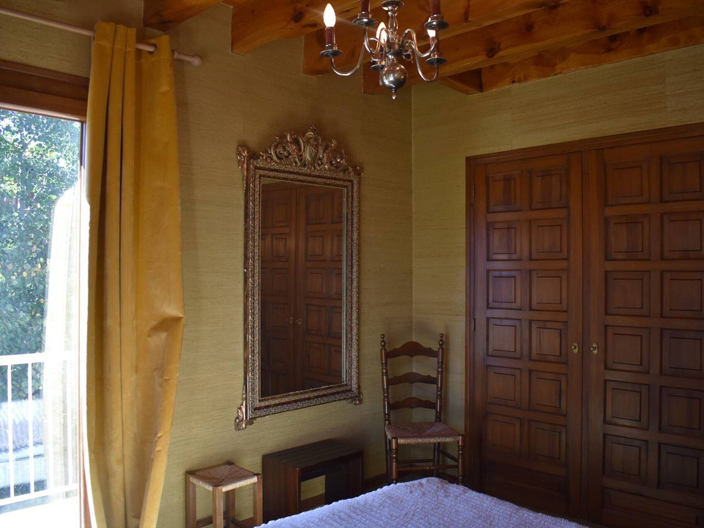 Une chambre avec une grande armoire en bois, un miroir, une chaise en bois et un lit.