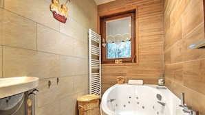 Un baño moderno con una bañera grande, un tocador de madera y un ventanal con vistas a árboles.
