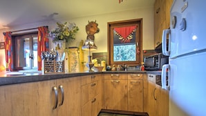 Una cocina con armarios de madera, microondas, refrigerador y ventana con cortina roja.
