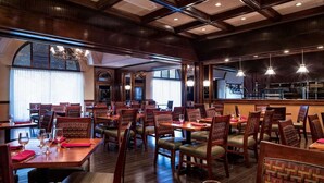 A restaurant with wooden tables and chairs, large windows, and hanging lights.