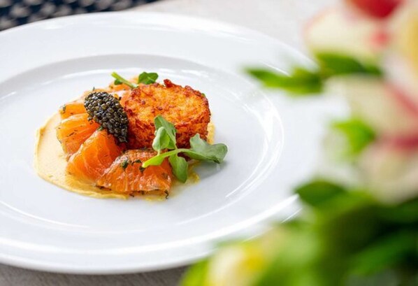 A white plate with a piece of salmon, a caviar dot, and some greens.
