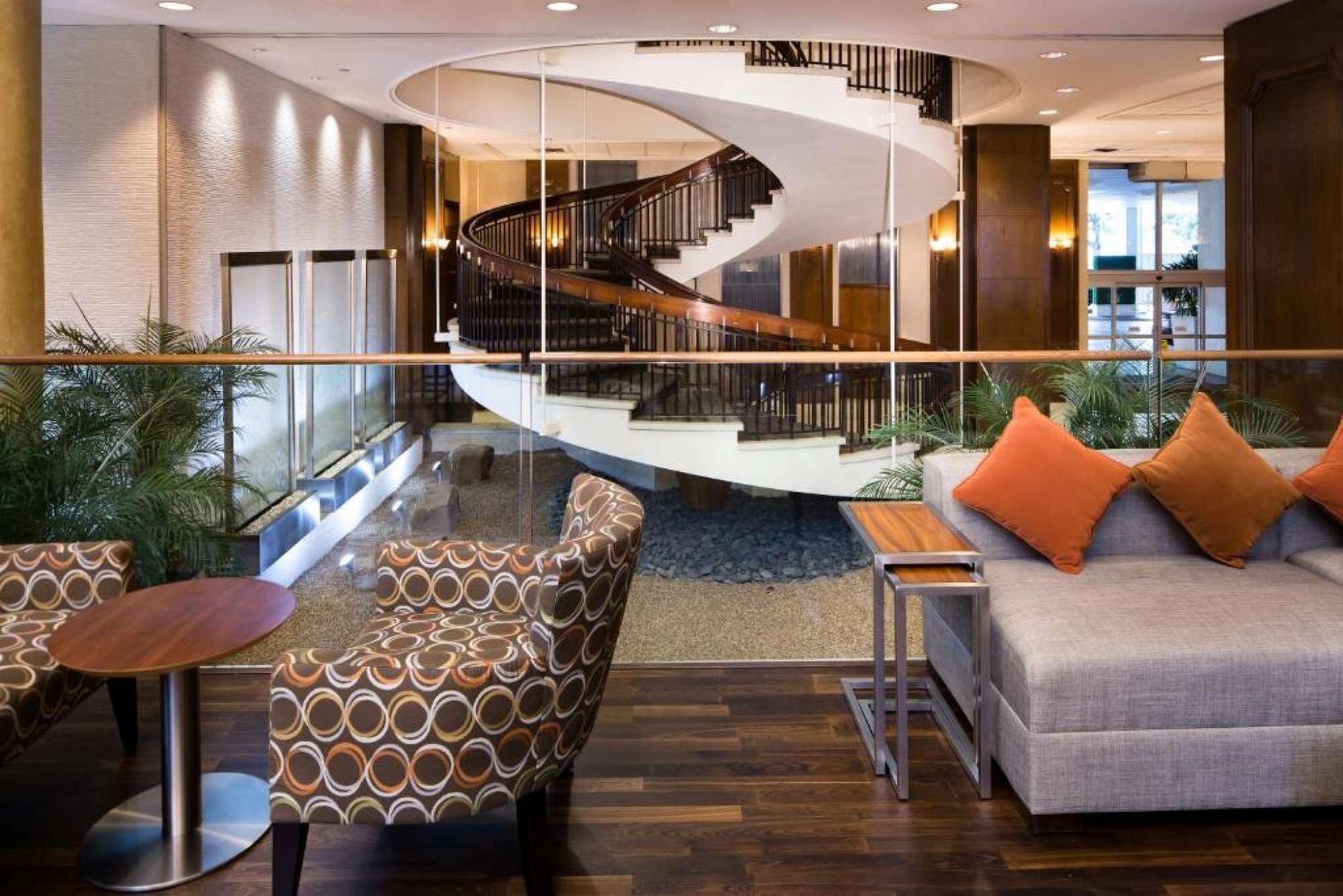 A modern lobby with a spiral staircase, seating areas, and a glass railing overlooking a lower level.
