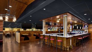 Eine Bar mit Holzhockern, einer Theke und einer Sitzgruppe mit Tischen und Stühlen.