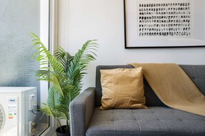 A living room with a grey sofa, a tan pillow, a potted plant, and a framed picture on the wall. - Family-friendly Apartment, Pool & Panoramic Views (Ñuñoa)