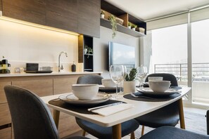 Uma sala de jantar moderna com uma mesa branca, cadeiras escuras e uma televisão de tela plana acima.