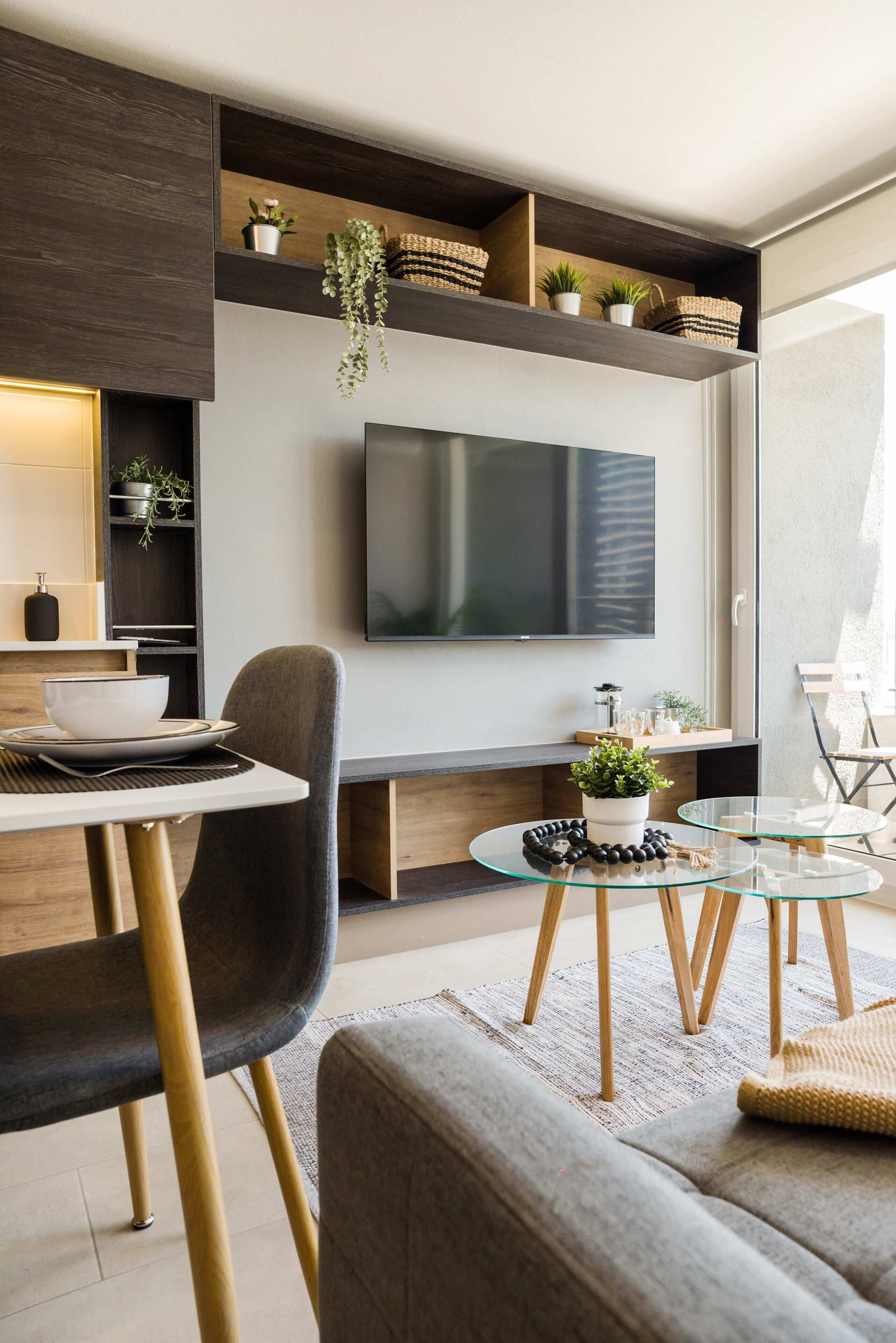 A modern living room with a flat-screen TV, a dining area with a bowl and plates, and a sofa with a glass coffee table.