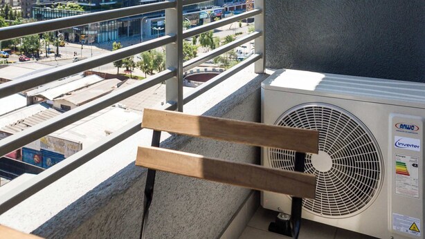 Ein Balkon mit Blick auf hohe Gebäude, einer Klimaanlage und einem Holgitter.