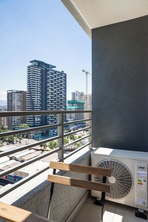 Ein Balkon mit Blick auf hohe Gebäude, einer Klimaanlage und einem Holgitter.