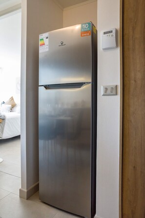 A modern stainless steel refrigerator with a digital control panel, located in a room with a wooden door and a white wall. - Family-friendly Apartment, Pool & Panoramic Views (Ñuñoa)