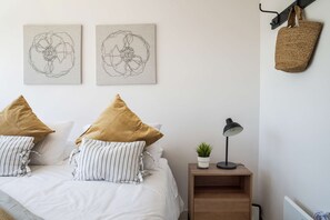 A neatly arranged bedroom with a bed, pillows, a nightstand with a lamp, a hanging basket, and two wall-mounted artworks. - Family-friendly Apartment, Pool & Panoramic Views (Ñuñoa)