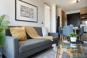 Ein modernes Wohnzimmer mit einem grauen Sofa, einem Glastisch und einem gerahmten abstrakten Kunstwerk an der Wand.
