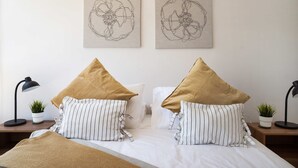 Ein ordentlich gemachtes Bett mit gestreiften Kissen und einer beigen Tagesdecke, flankiert von zwei an der Wand befestigten abstrakten Kunstwerken.