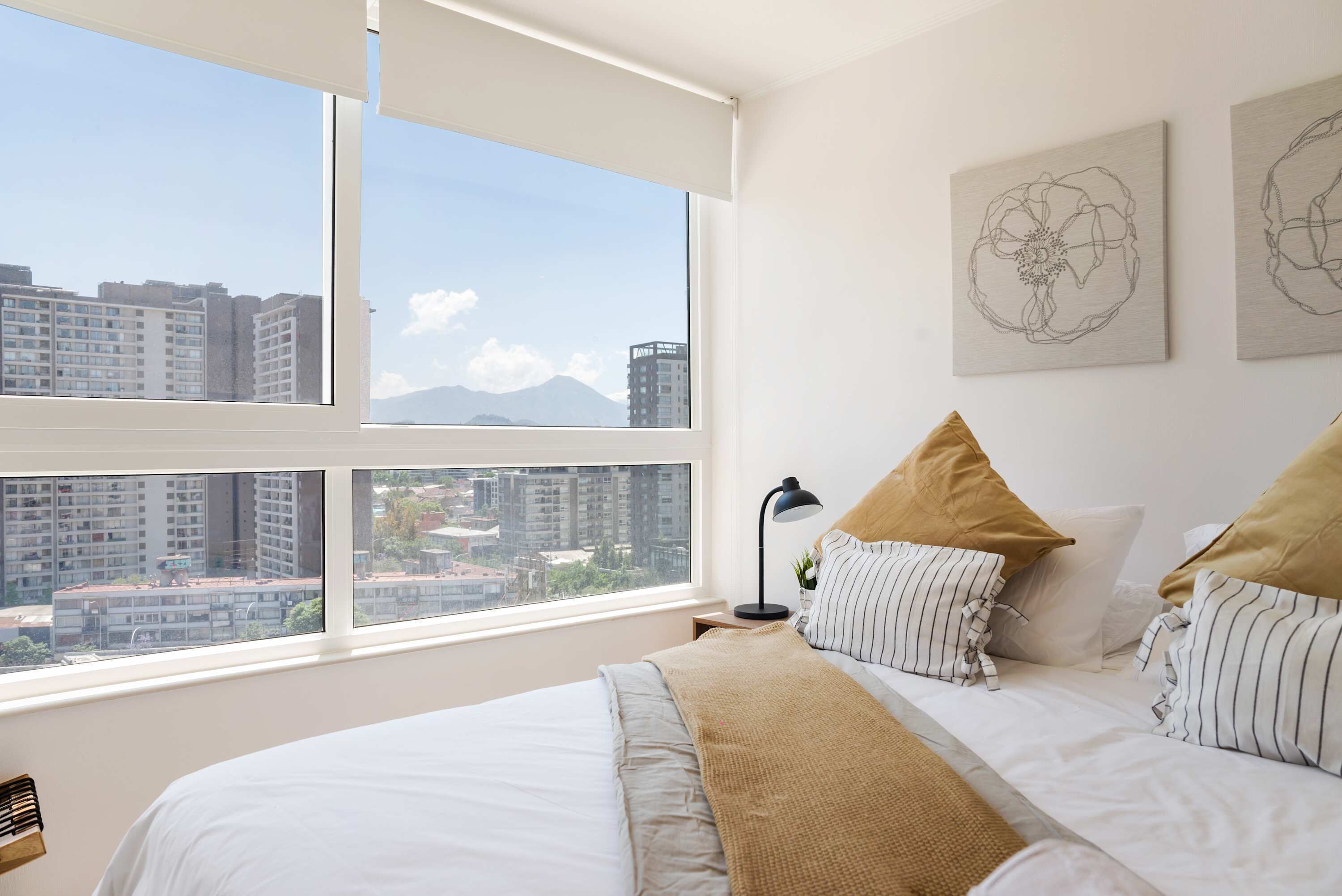 A bedroom with a large window, a bed with striped pillows, and two wall art pieces.