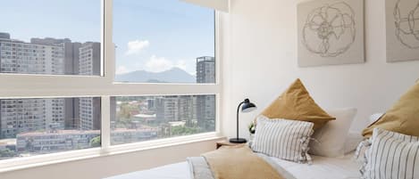 Un dormitorio con un ventanal grande, una cama con almohadas a rayas y dos cuadros en la pared.