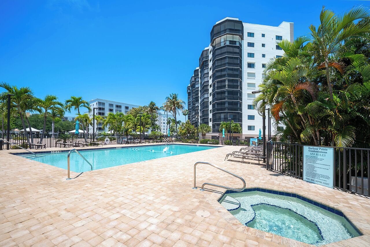 Een zwembad met betegeld zonnedek, een jacuzzi en een bord met de tekst 'Harbour Pointe Condominiums SPA RULES'.