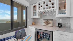 Una cocina con armarios blancos, una vinera empotrada, una licuadora y vistas al exterior.