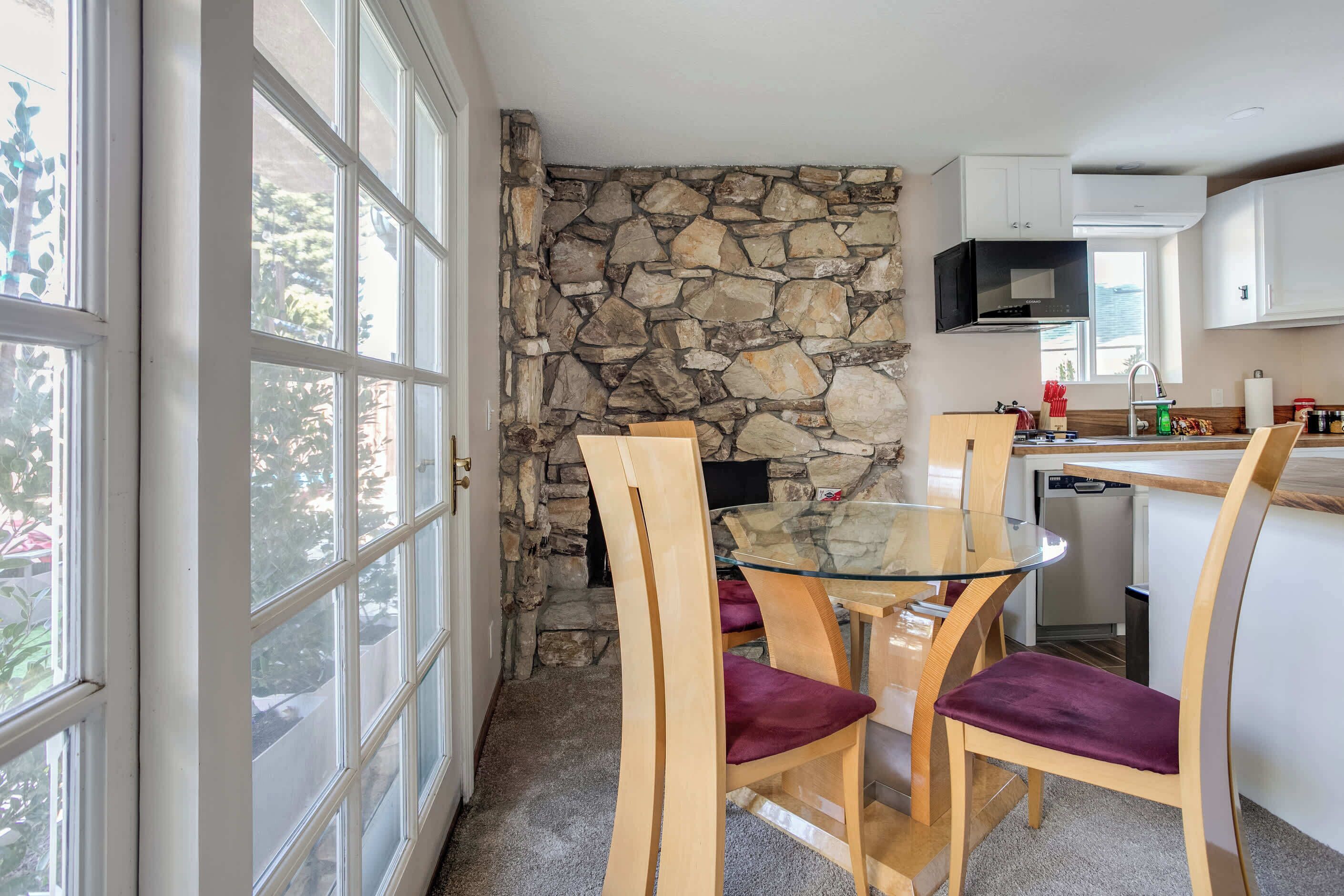 Una cocina con pared de piedra, mesa de vidrio y sillas moradas.