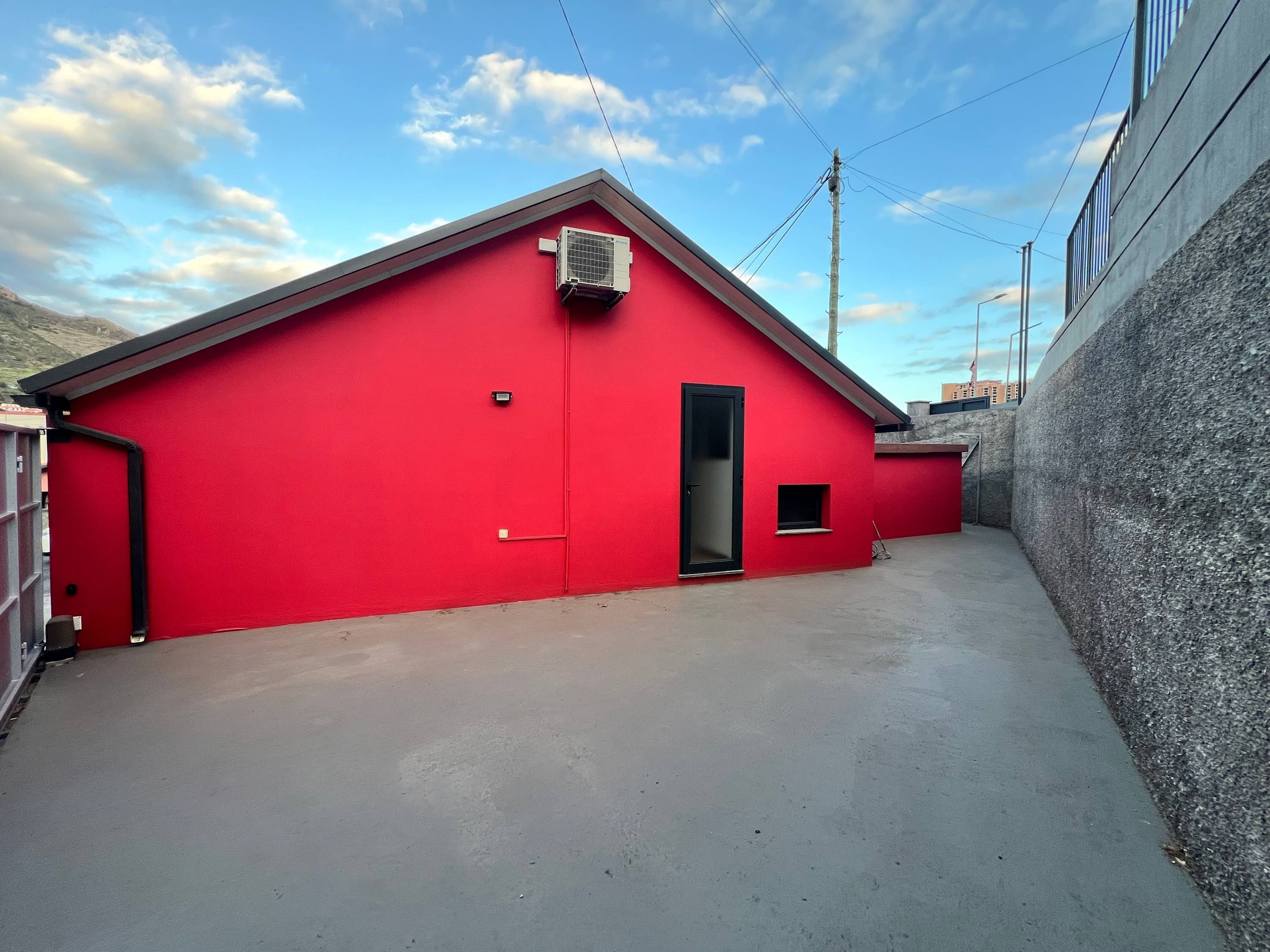 A red building with a flat roof, a small door, and an air conditioning unit.