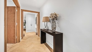 Een hal met een houten vloer, een donkere console en een vaas en lamp, en een spiegel aan de muur.