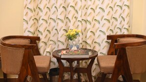 A room with a round wooden table, two upholstered chairs, a vase with yellow flowers, and a patterned curtain. - Hotel Virasat Haveli (Sawai Madhopur)