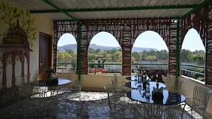 A covered outdoor seating area with tables and chairs, a decorative wall, and a view of a mountainous landscape. - Hotel Virasat Haveli (Sawai Madhopur)