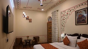 A hotel room with a bed, a TV, a small table with chairs, and a decorative ceiling. - Hotel Virasat Haveli (Sawai Madhopur)