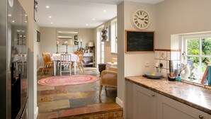 A kitchen with a clock, a dining area with chairs and a table, and a window with a view.