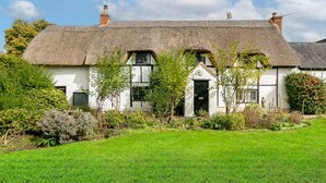 A traditional white cottage with a thatched roof, surrounded by a well-maintained garden and a green lawn.