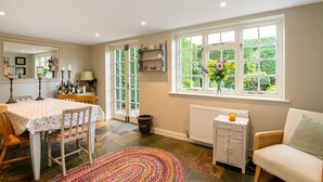 A dining area with a table and chairs, a window with a view of greenery, a radiator, and a wicker chair.
