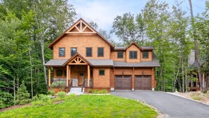 A two-story wooden house with a front porch, garage, and surrounded by trees. - Riverfront Luxury at South Peak, Hot Tub, Fire Pit, Sleeps 12 (Lincoln)