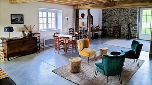 A spacious living area with a high ceiling, rustic wooden beams, a stone wall, and a large window providing natural light. - Charming Basque house with swimming pool (Souraïde)