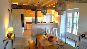 A spacious living area with a wooden dining table, benches, and a kitchen in the background. - Charming Basque house with swimming pool (Souraïde)