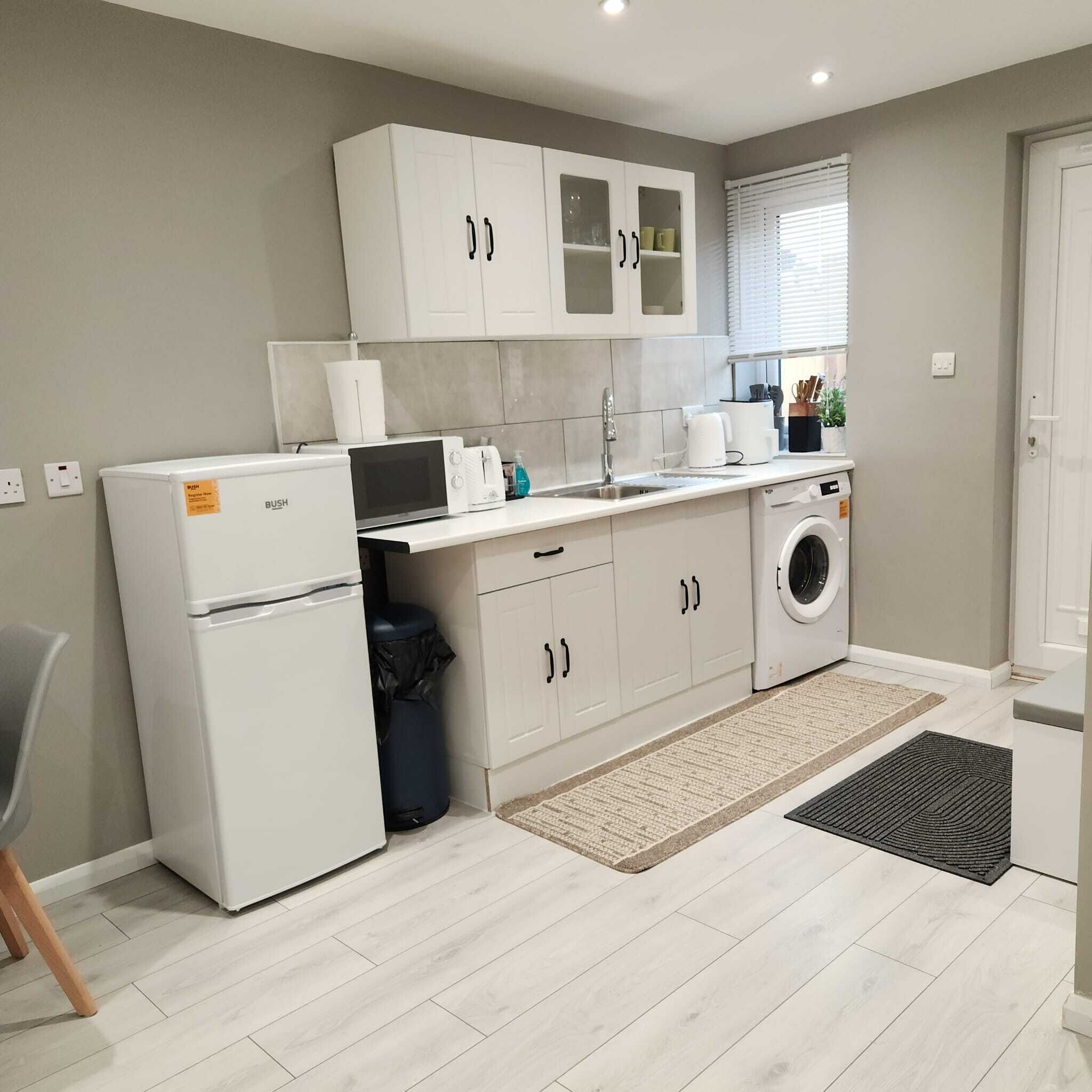 A modern kitchen with white cabinets, a built-in microwave, a washing machine, and a small trash bin.