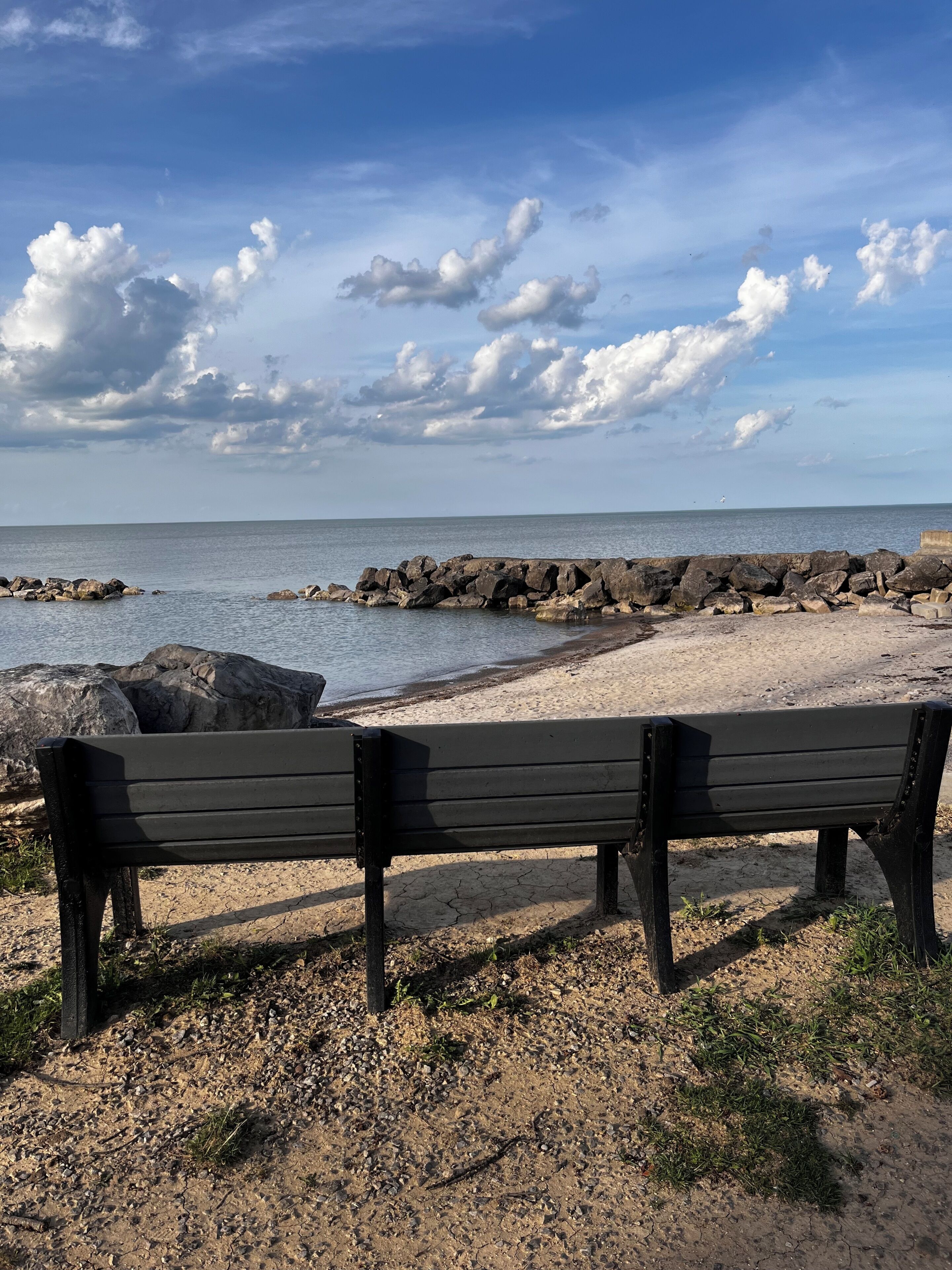 Une plage avec deux bancs en bois donnant sur la mer, une digue rocheuse et un ciel dégagé.