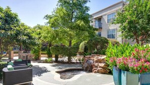 A courtyard with outdoor seating, a small waterfall, and lush greenery. - Landing Apartments - North Dallas (Dallas)