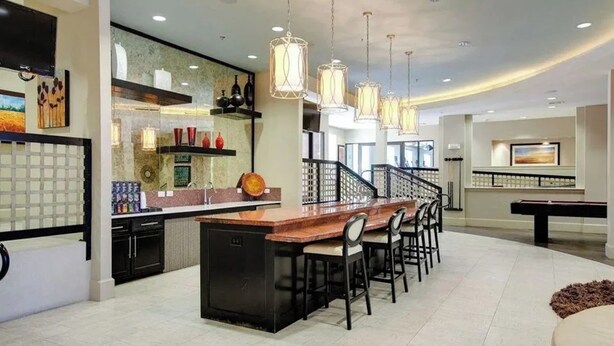 A modern kitchen with a central island, bar stools, pendant lighting, and a pool table. - Landing Apartments - North Dallas (Dallas)