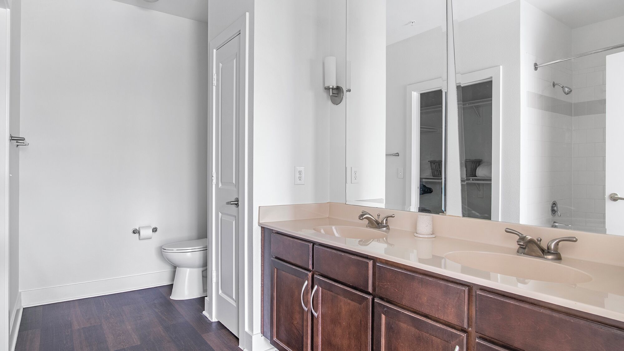 A bathroom with a double sink, dark wood cabinets, a large mirror, and a toilet.