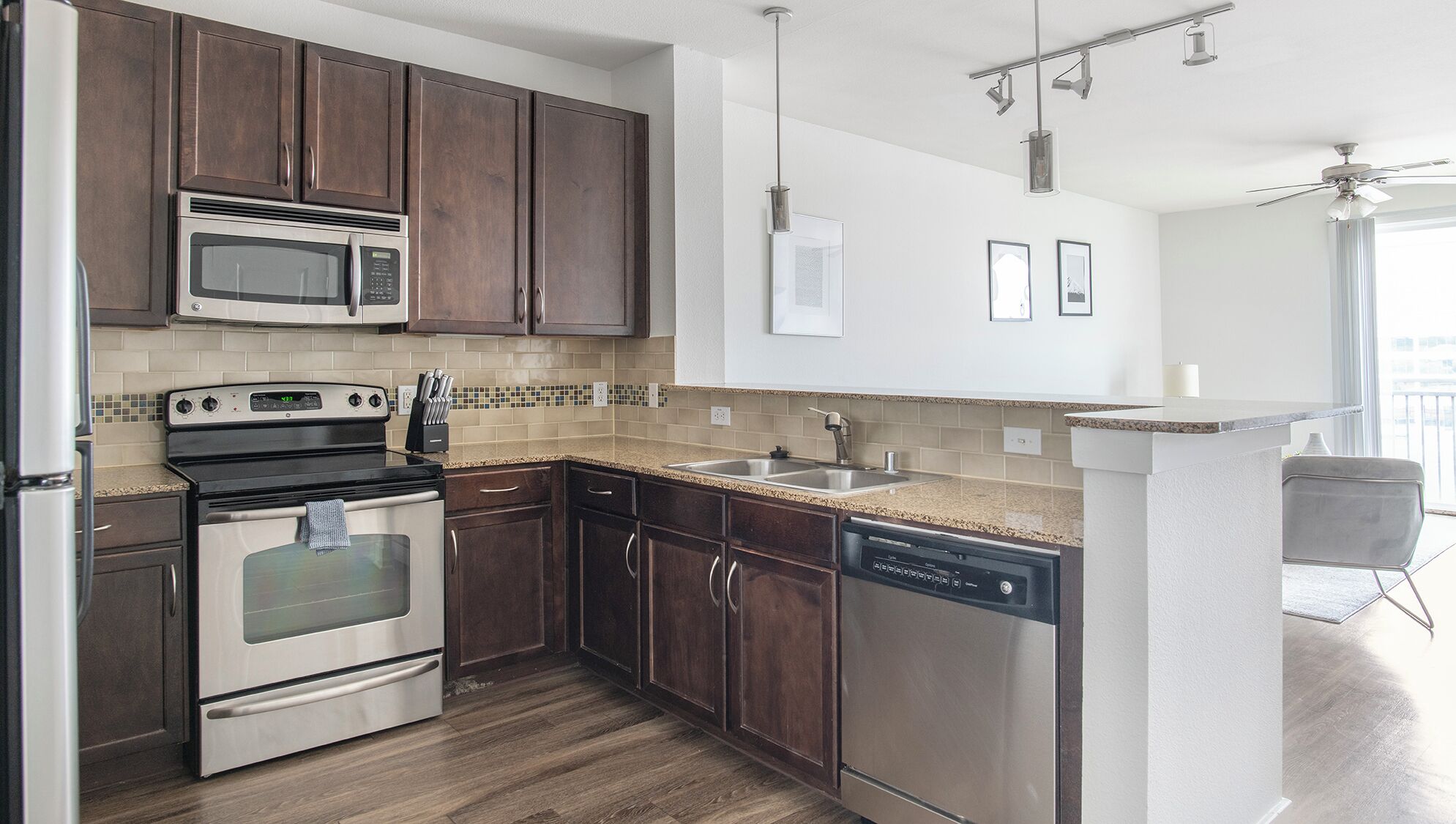 A modern kitchen with dark wooden cabinets, stainless steel appliances, a tiled backsplash, and a built-in dishwasher.