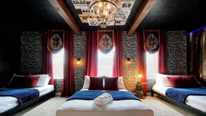 Hotellihuone, jossa on suuri sänky, kaksi pienempää sänkyä, punaiset verhot, kiviseinät ja kattokruunu.